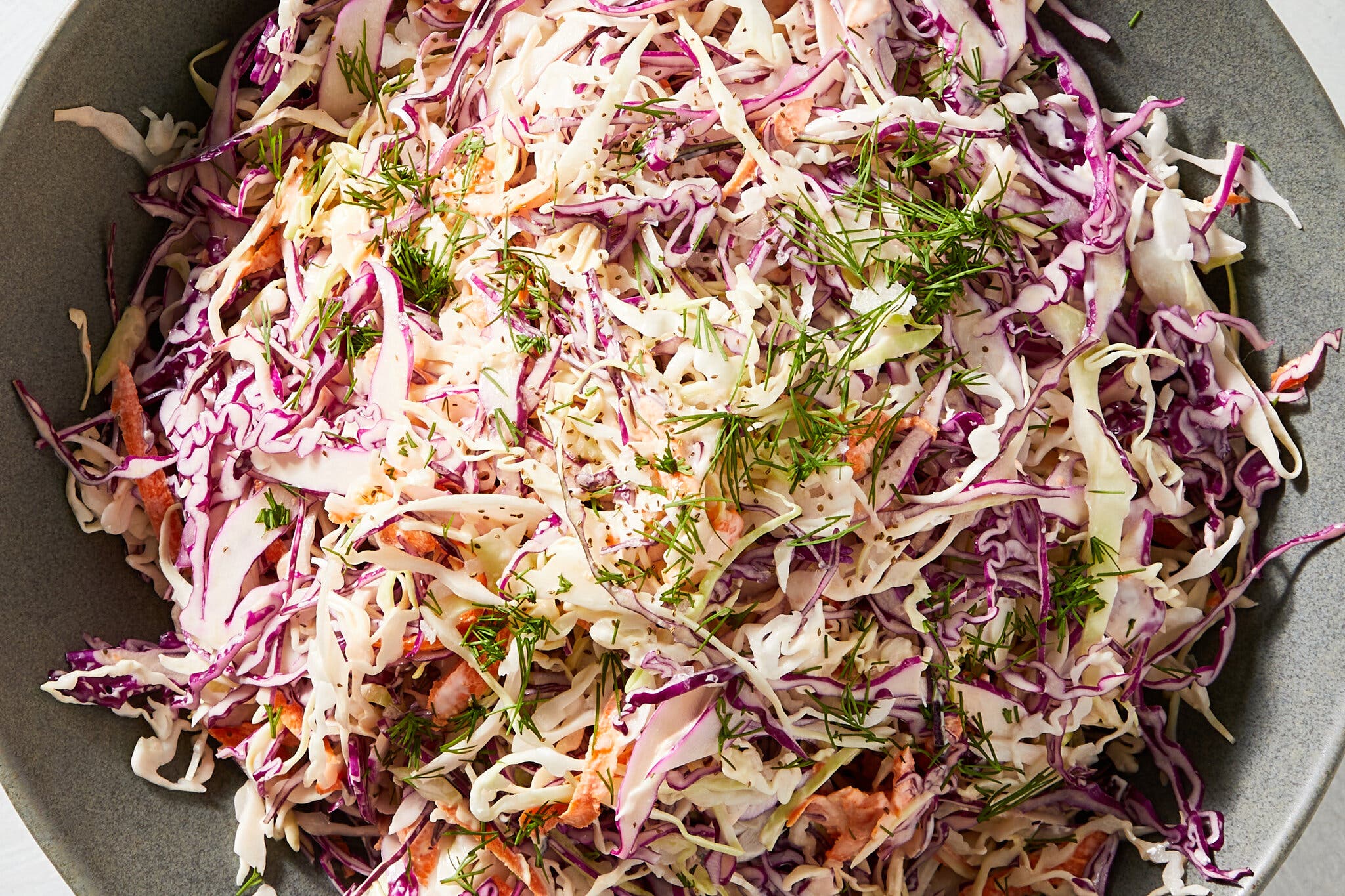 An overhead image of a gray bowl holding shredded cabbage topped with herbs.