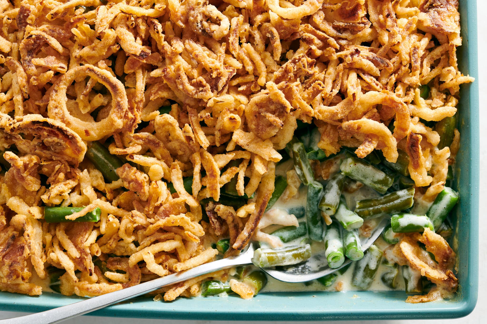 An overhead image of a 9-by-13-inch baking dish filled with green bean casserole and topped with crisp French-fried onions. A scoop is taken out from one corner to expose the inside.
