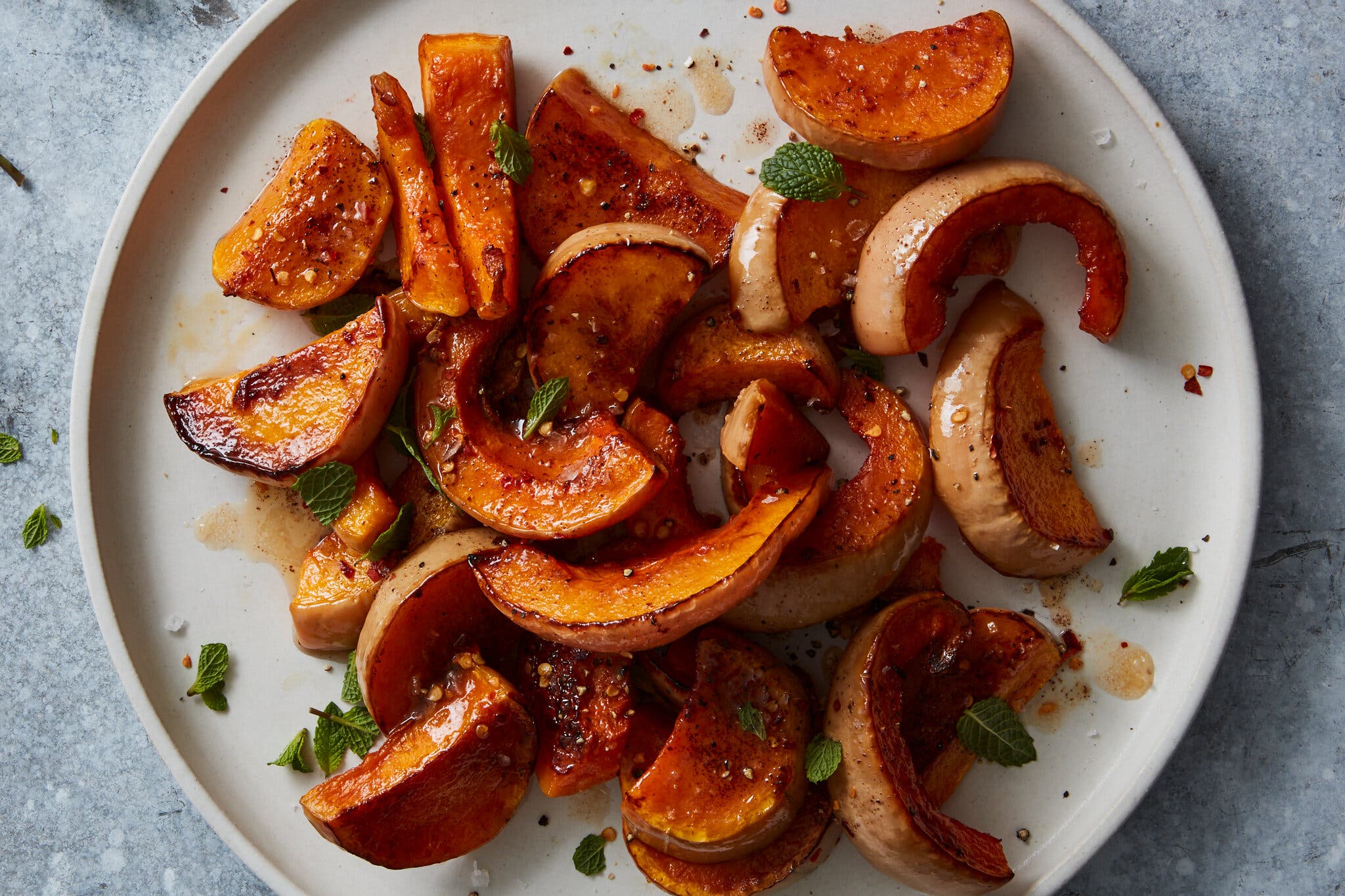 An overhead image of a white plate with roasted butternut squash and dotted with torn mint leaves.