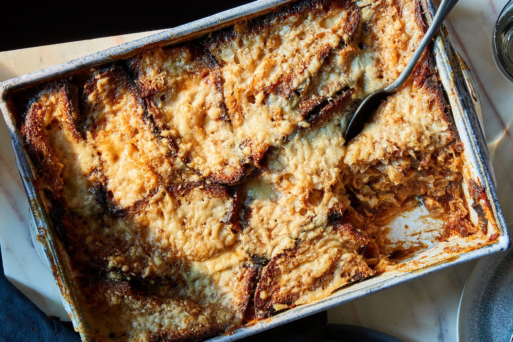 An overhead shot of a baking dish full of panade, topped with soft bread and melted cheese. There is a spoon in the dish