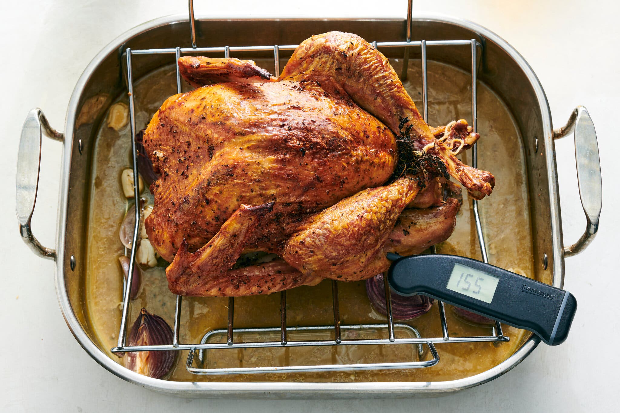 An overhead image of a cooked turkey with a thermometer inserted into the thickest part of the thigh.