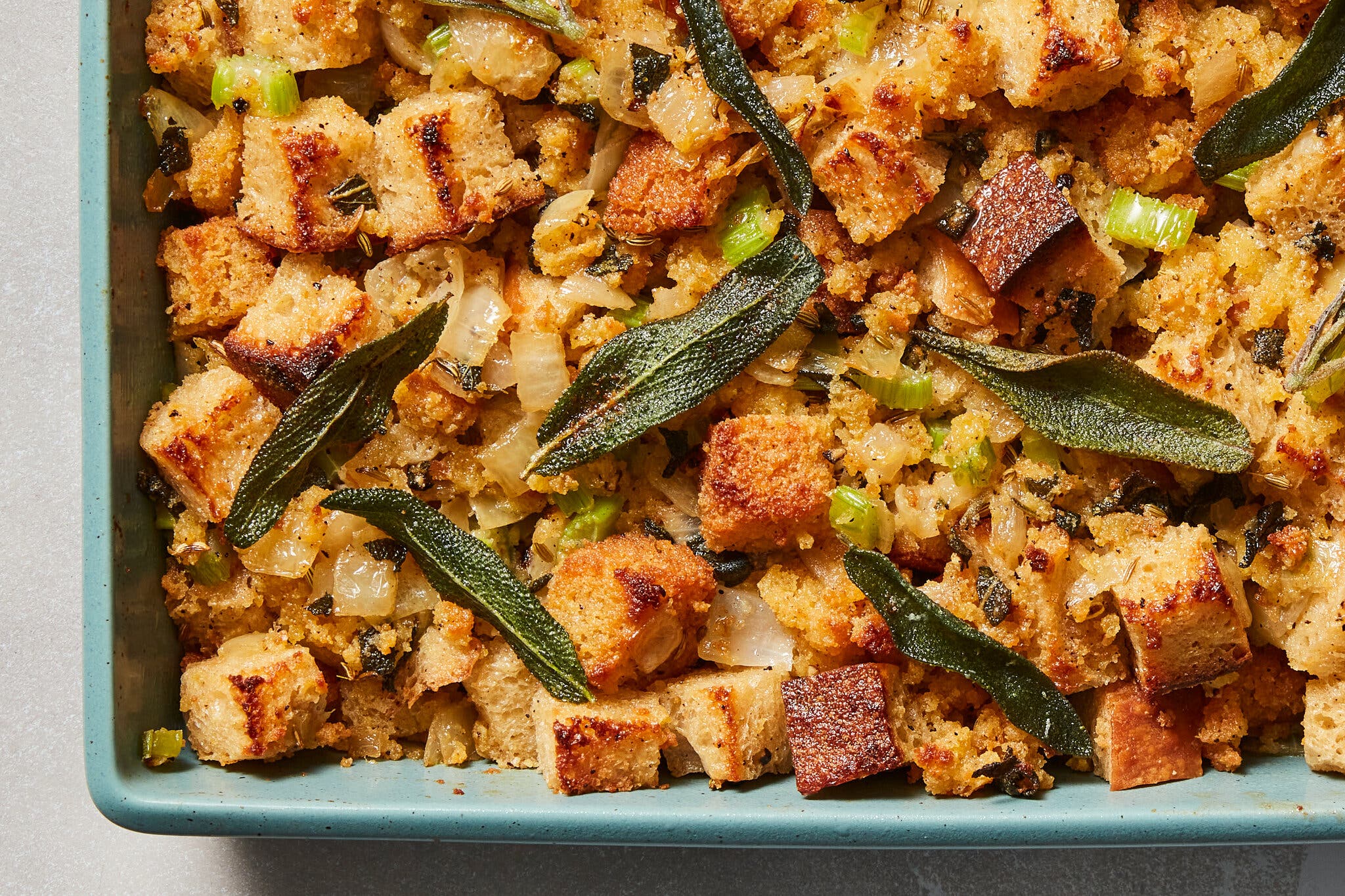 An overhead image of a baking dish filled with burnished cubed bread studded with onion and celery and finished with crisp sage leaves.