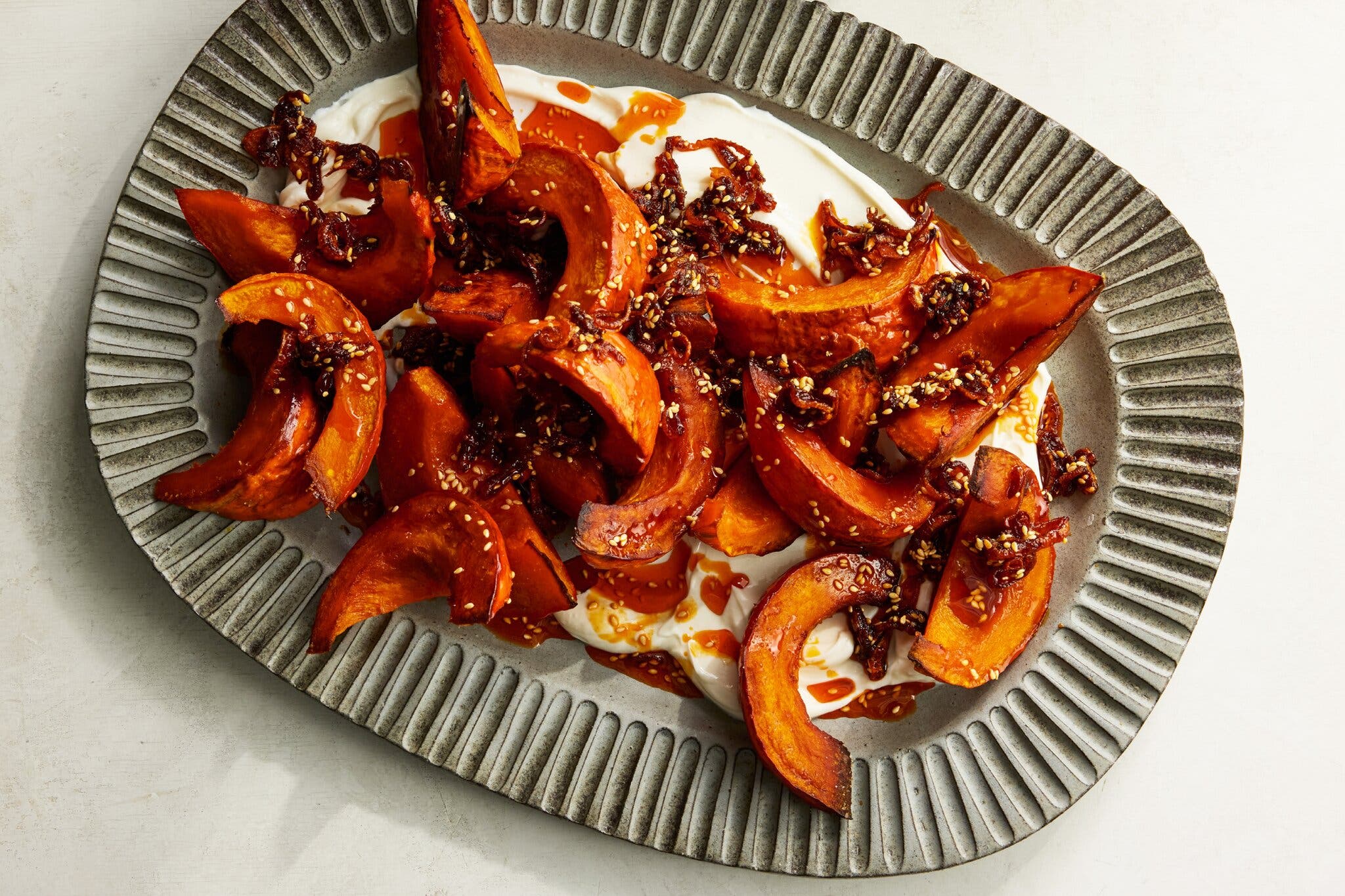 Slices of roasted orange squash with a dark, sticky glaze and sesame seeds.