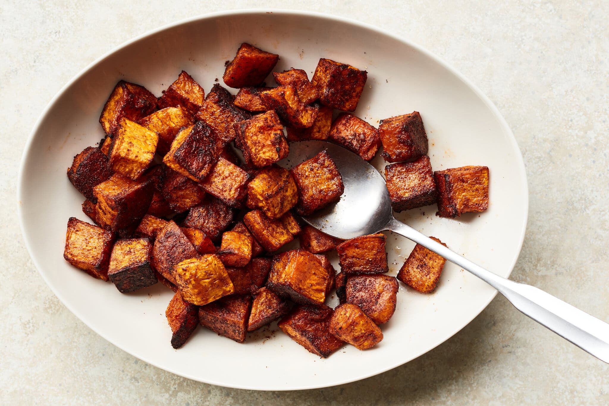 An overhead image of a white oval platter filled with chunks of roasted butternut squash coated with chili powder and cayenne.