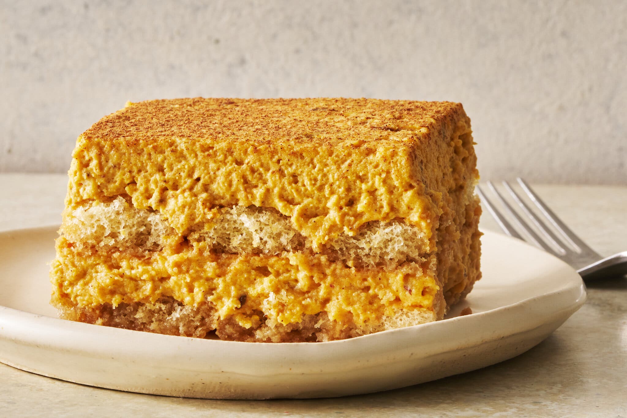 A side shot of a slice of pumpkin tiramisu on a plate. There is a fork in the background.