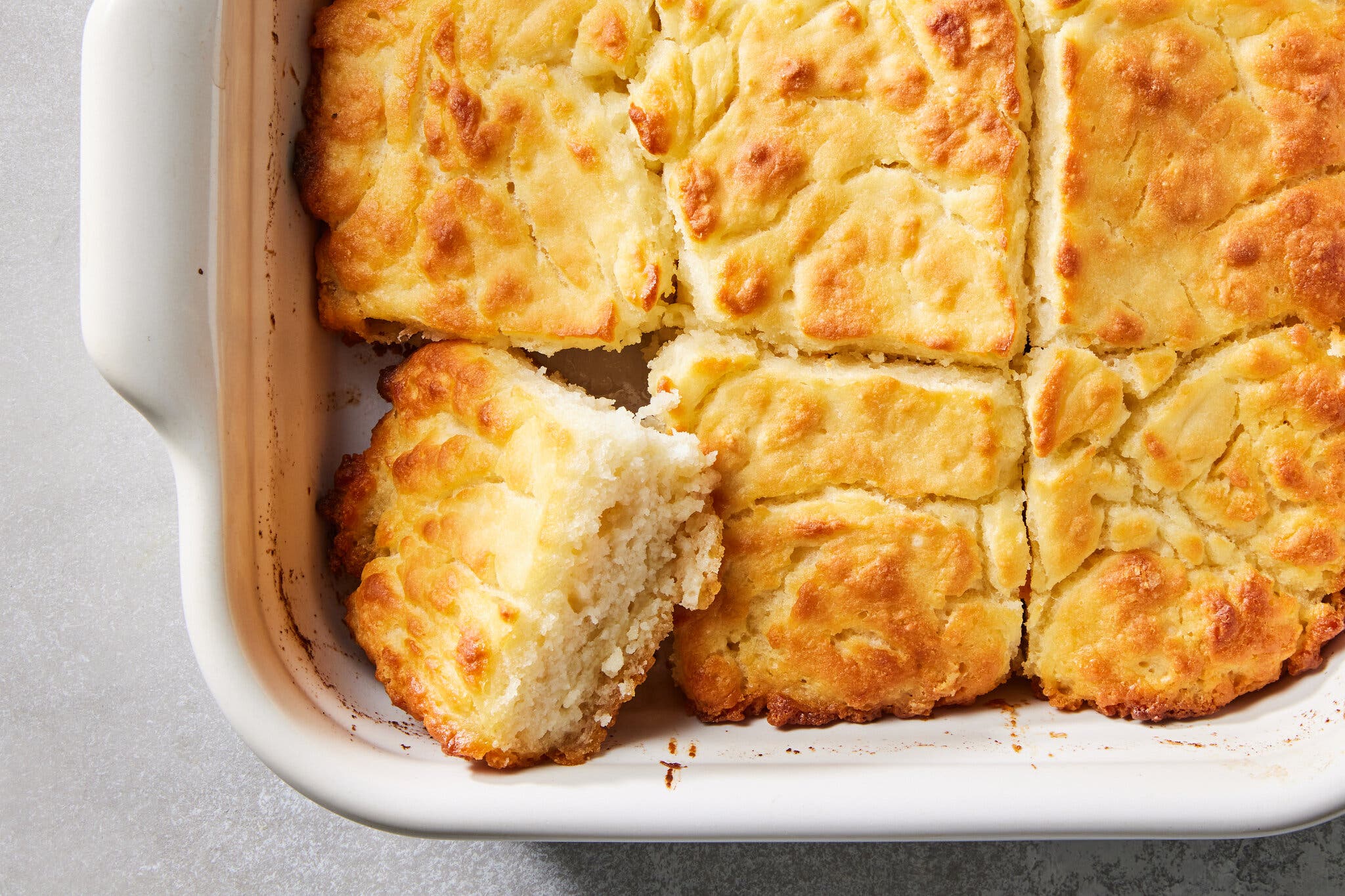 An overhead shot of a baking dish with butter swim biscuits. The corner piece is turned up to show the inside of the biscuit.