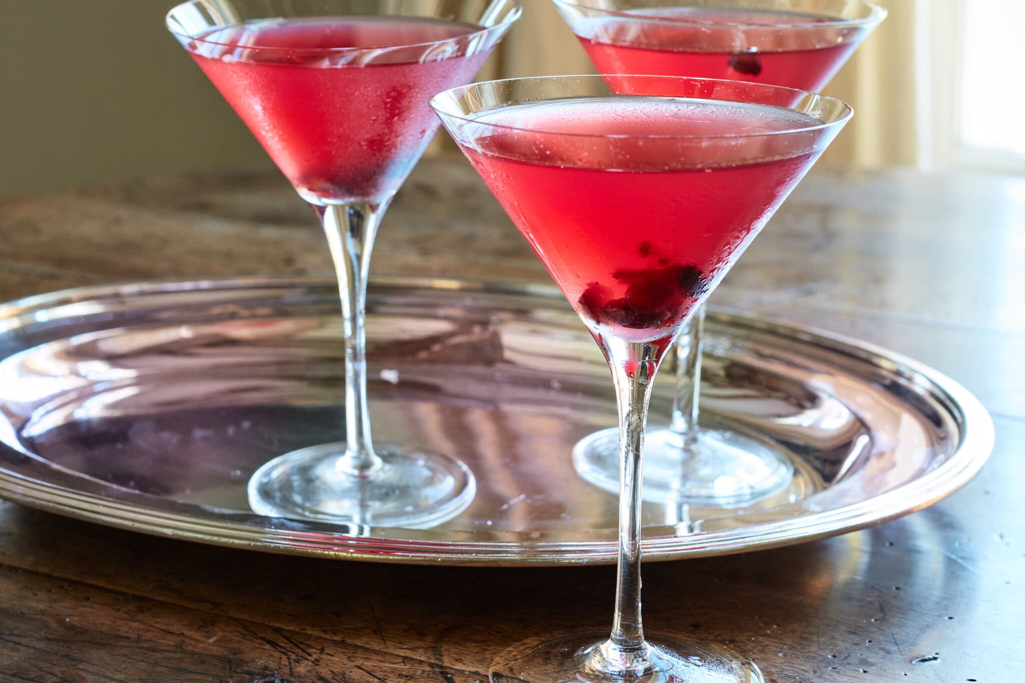 A side shot of three cranberry martinis, two of which are sitting on a silver tray.