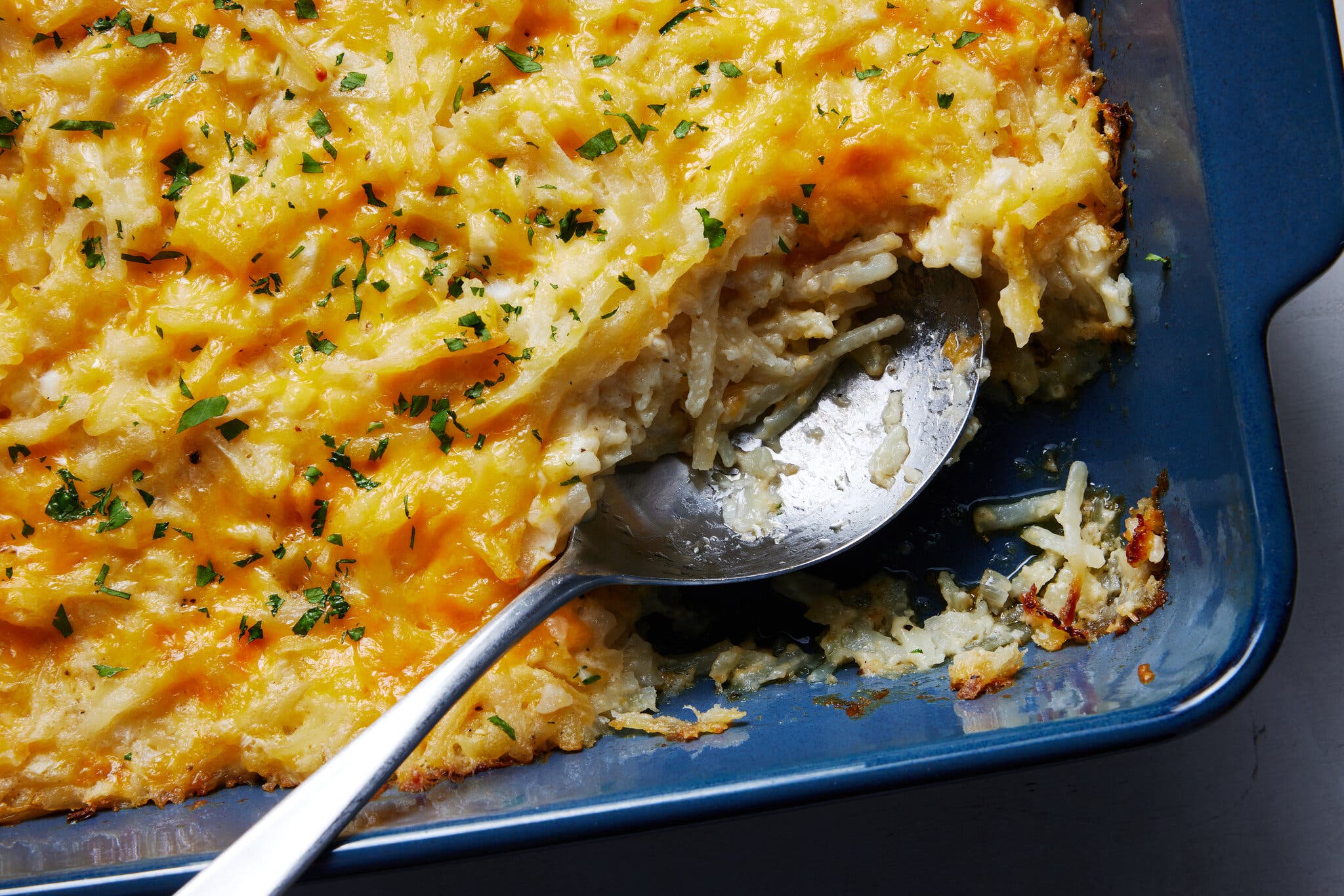 An overhead image of a hash brown casserole, with a cheesy top, baked into a blue ceramic dish.