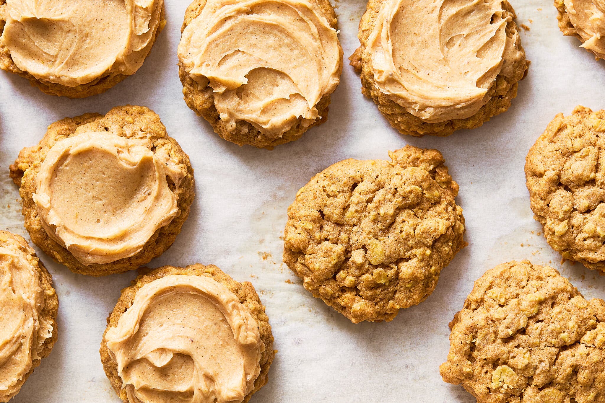 Craggy oatmeal cookies are photographed from overhead, some topped with a swirled frosting.
