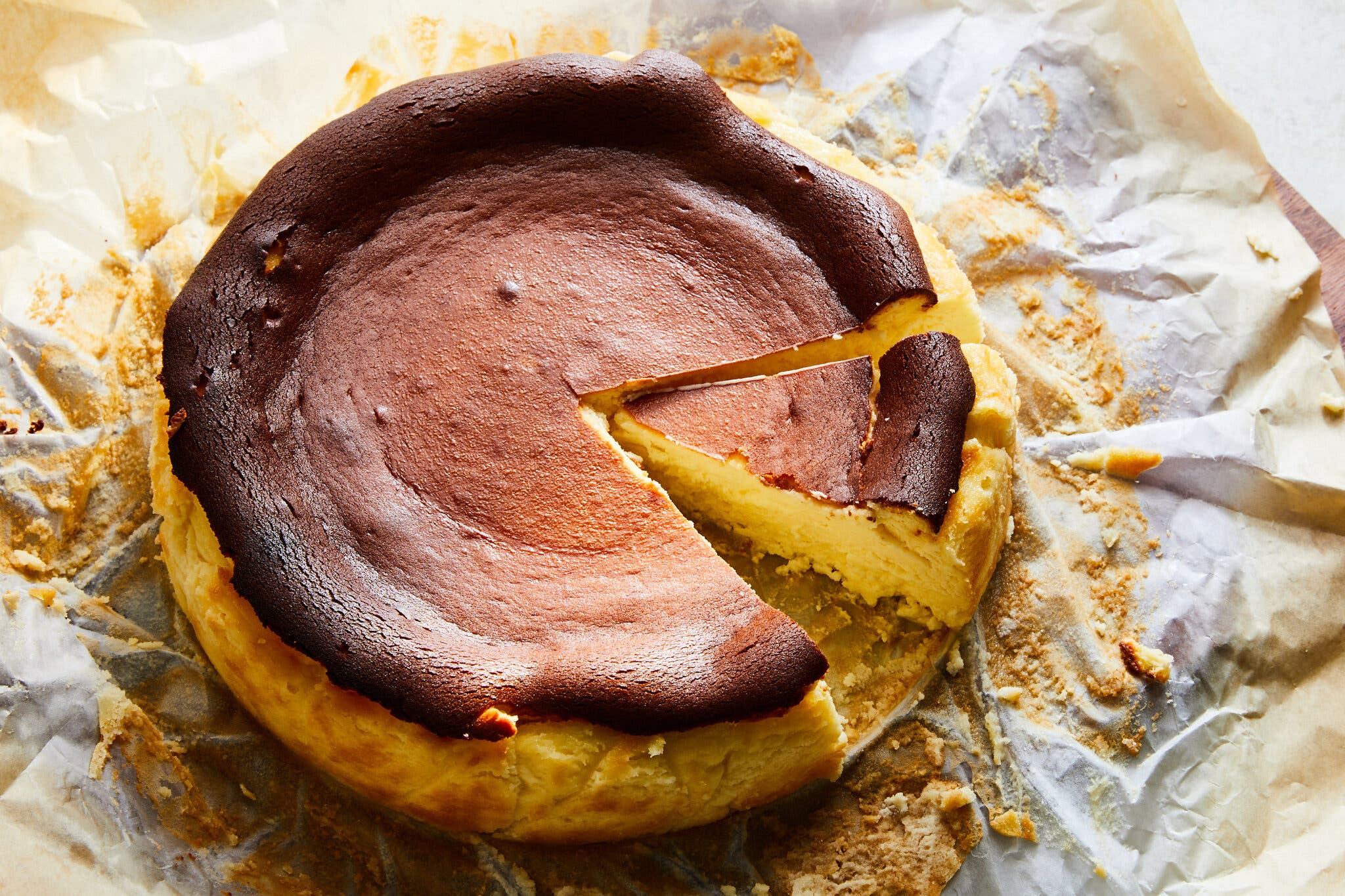A burnished cheesecake with a gorgeously cratered top sits on top of parchment paper, with a slice ready to be taken out.