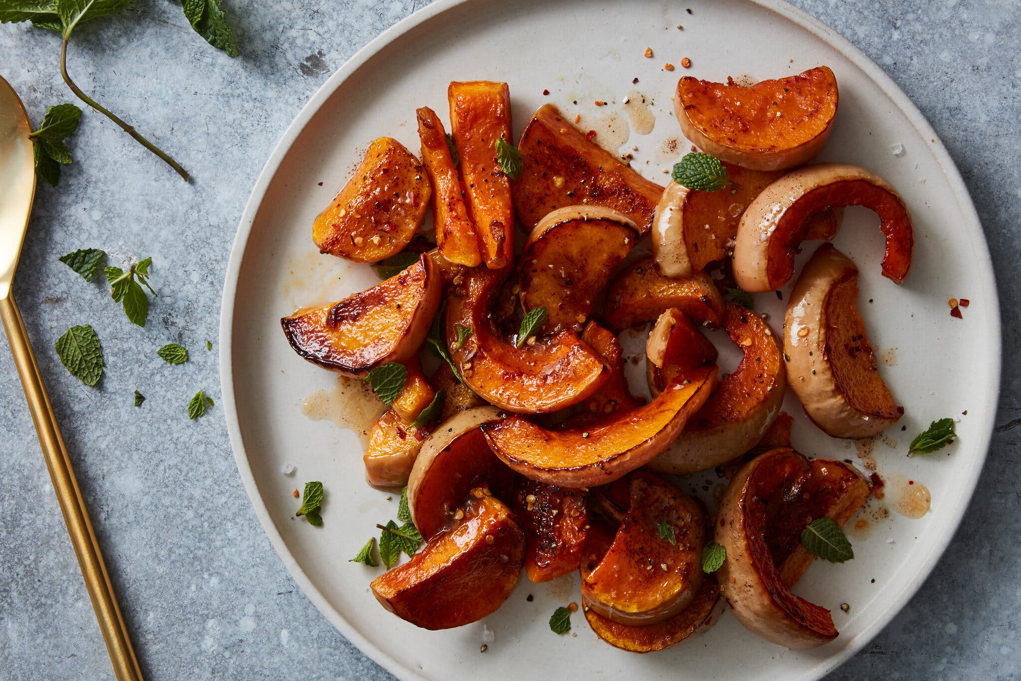 An overhead image of a round white plate filled with roasted butternut squash wedges scattered with brown butter and fresh herbs. 