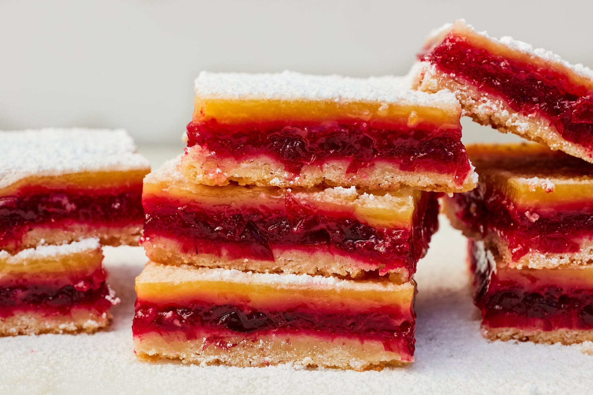 Eight cranberry lemon bars are shot from the side to reveal a cookie base topped with cranberry and lemon fillings.