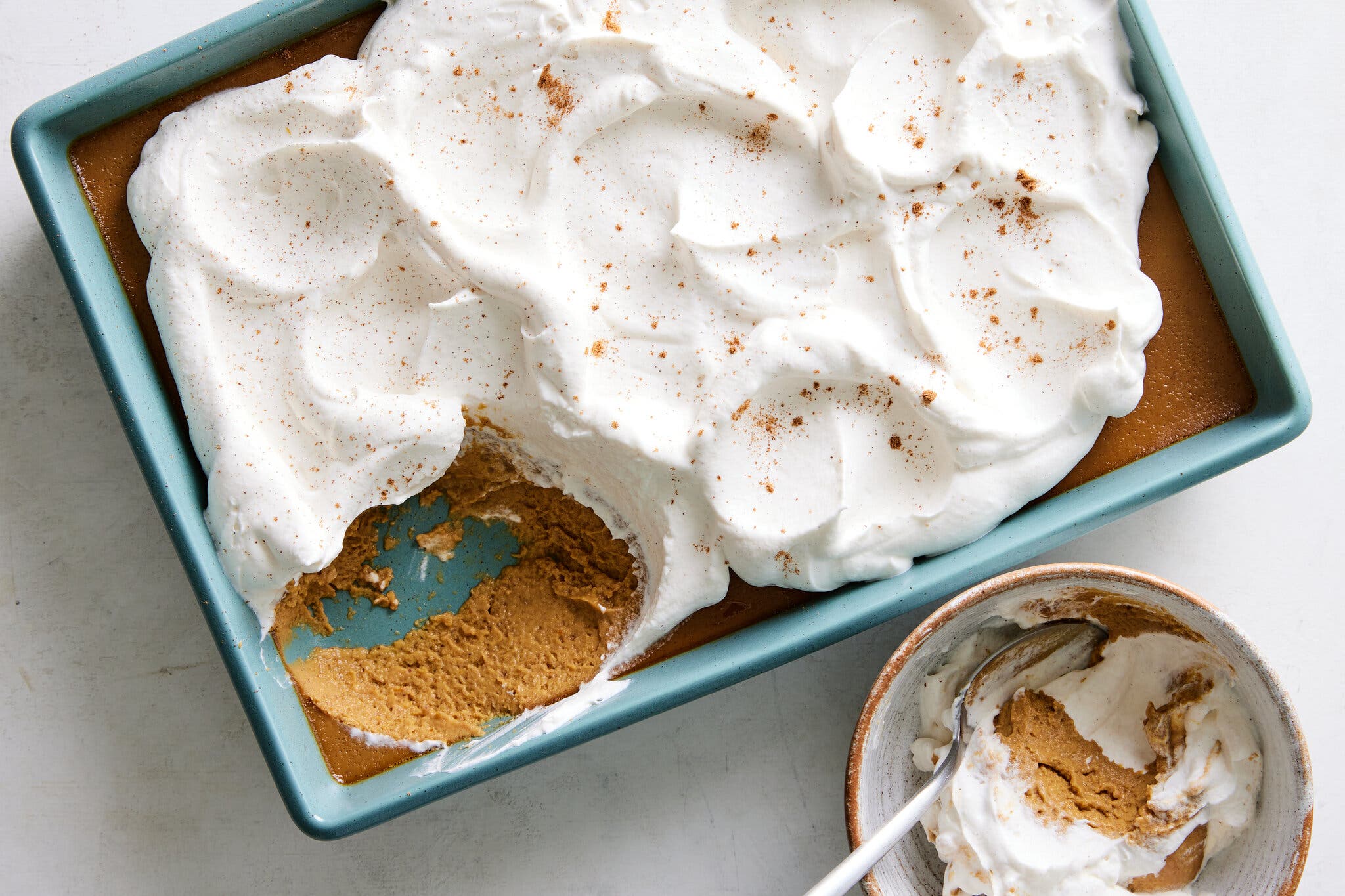 An overhead image of a blue baking dish filled with pumpkin butterscotch pudding and topped with whipped cream. A serving sits off to one side.