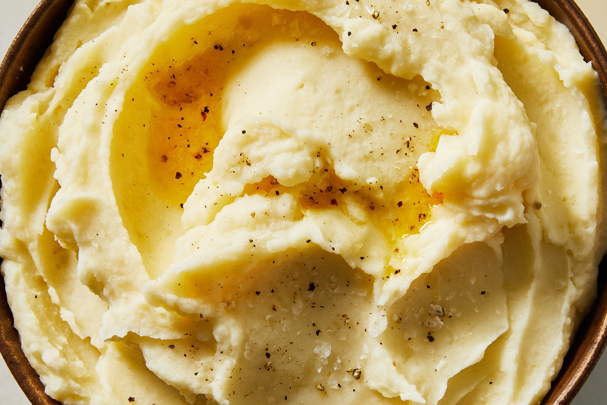 A close-up image of swirled mashed potatoes, speckled with pepper.