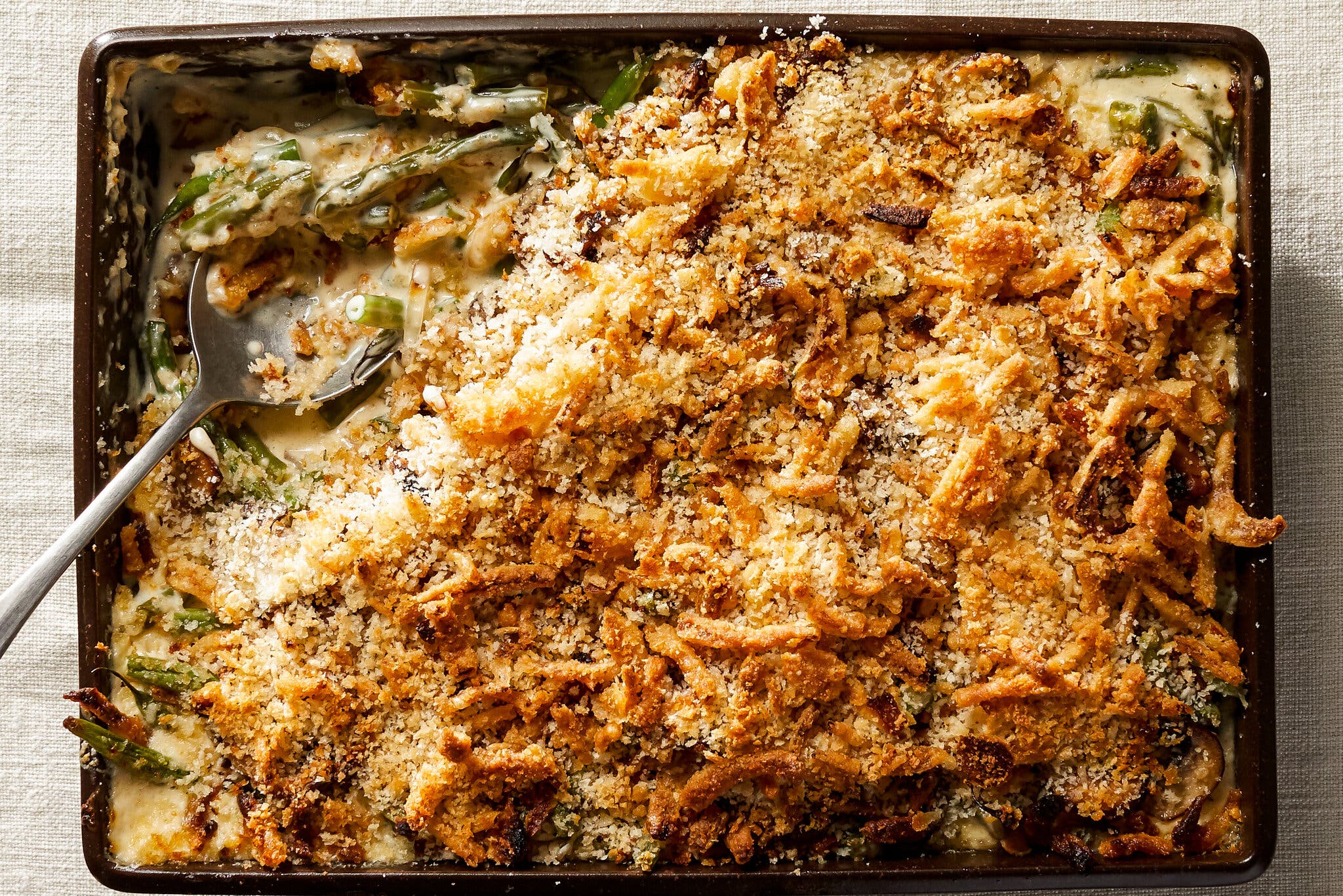 An overhead shot of a baking dish full of green bean casserole, topped with bread crumbs and fried onions.