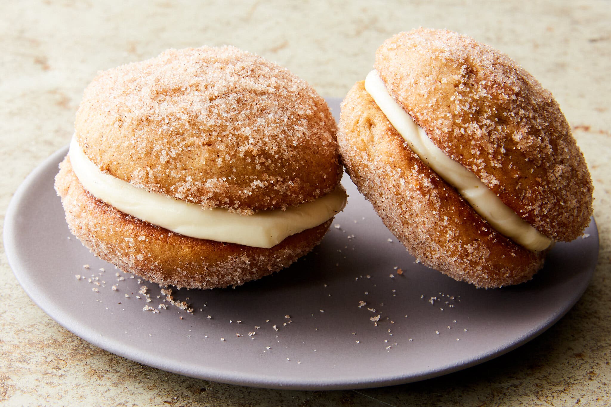 Two apple cider whoopie pies with a layer of cream cheese filling, on a plate.