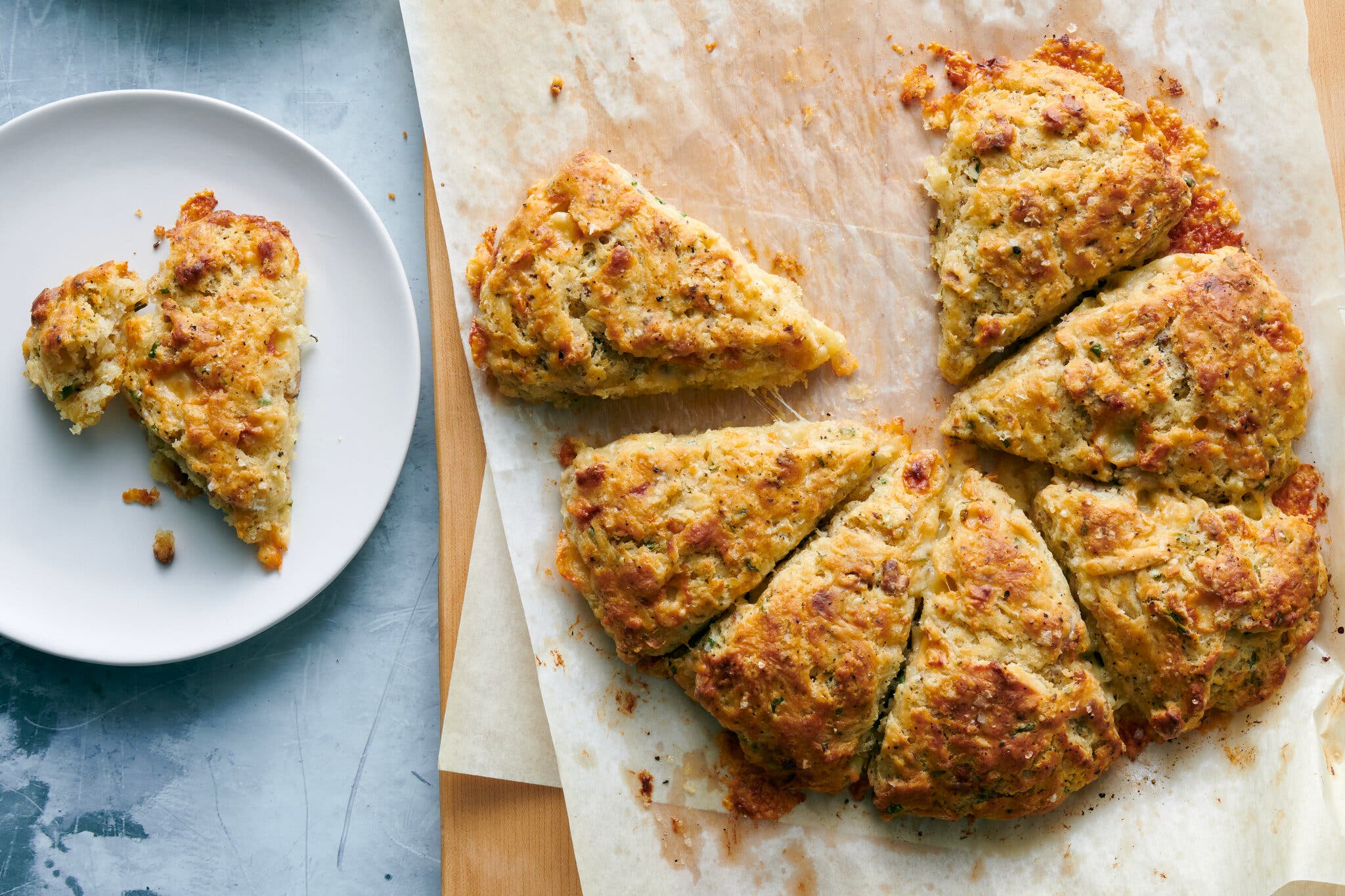 An overhead shot of a wheel of scones sitting on parchment paper. To the left, one of the scones sits on a plate.